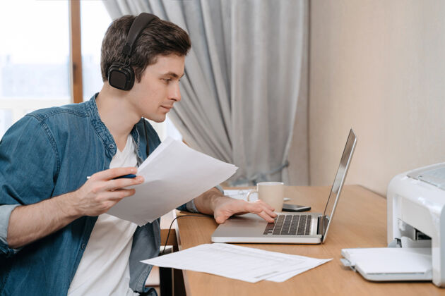 学生室内拍摄的年轻白种人商人在办公桌旁用手提电脑拿着一些文件房子在线学习社会距离
