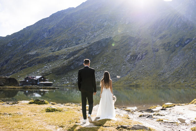 自然在日出的映衬下 坐在山中湖边的不可辨认的新郎和新娘的全长后视图浪漫一起妻子