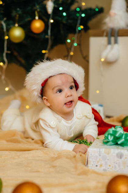 新可爱的微笑着的婴儿躺在圣诞树下和孩子们玩耍礼物.圣诞节还有新年庆祝活动坐着快乐玩