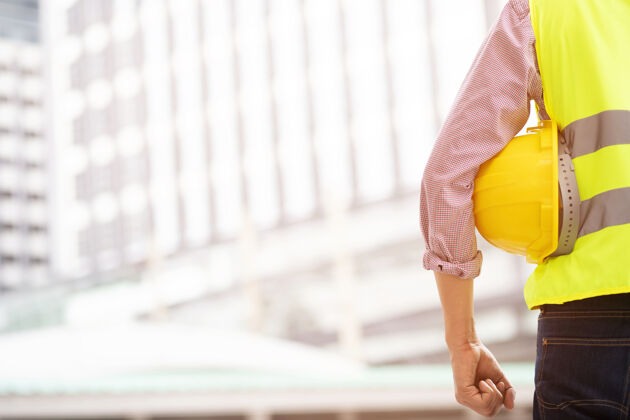 建筑工程男施工人员手持黄色安全帽 穿着反光服 工作安全室外操作建筑物的名称承包商工作计划