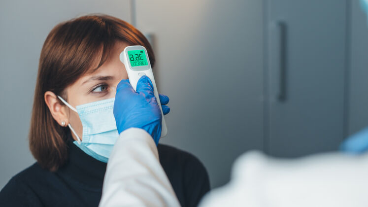 专业人员一位戴着手套的白人医生在会诊时戴着口罩测量病人的体温检查冠状病毒疾病
