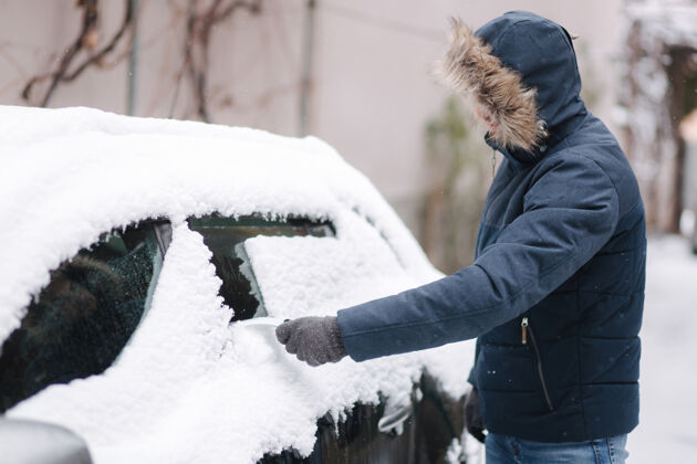 冷冻冬天 一个年轻人在车库附近清理汽车挡风玻璃上的雪结冰移除户外