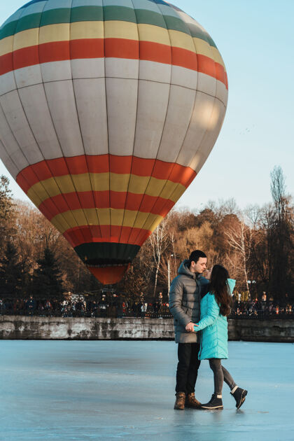 户外新娘和新郎在冰冻的湖面和城市公园里飞行的气球的背景下浪漫热历史