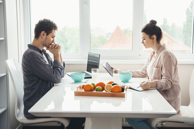 烹饪一对高加索夫妇坐在桌子旁 一边吃麦片 一边用笔记本电脑工作在线商务女性健康习惯