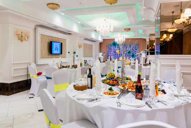 大厅在明亮的白色豪华宴会厅内的有盖餐桌上举行婚礼活动优雅盘子葡萄酒