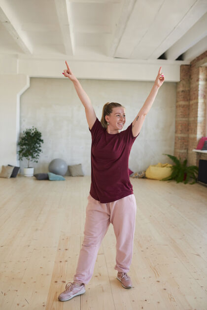 放松穿着运动服的年轻女子举手微笑着在舞蹈室锻炼放松锻炼瑜伽活力