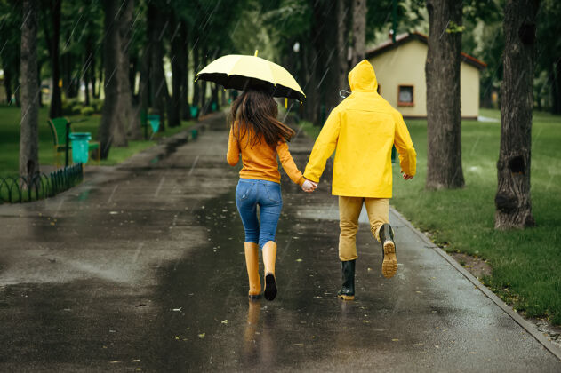 公园雨天 一对恋人撑着伞在公园散步戴曼穿着胶靴的女人走在小路上 小巷里天气潮湿快乐湿拥抱