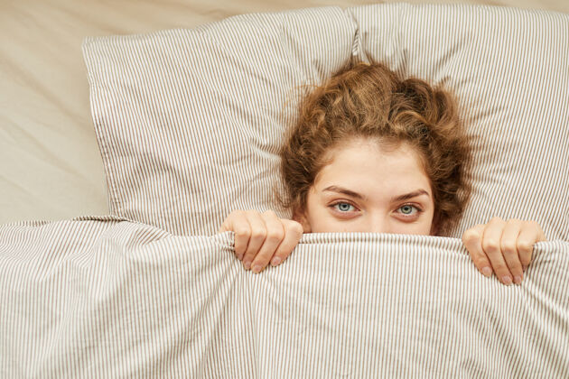 毛毯特写镜头中的年轻女子正躺在床上看前面的毯子下面隐藏迷人的女性睡眠
