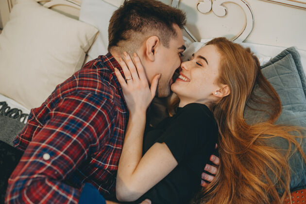 激情一对美丽的年轻夫妇在家中面对面地倚在床上 拥抱着 笑着的侧视图微笑拥抱床
