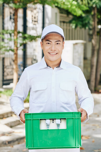 携带快乐帅气的越南送奶工的画像 背着绿色的塑料牛奶箱板条箱盒子亚洲人