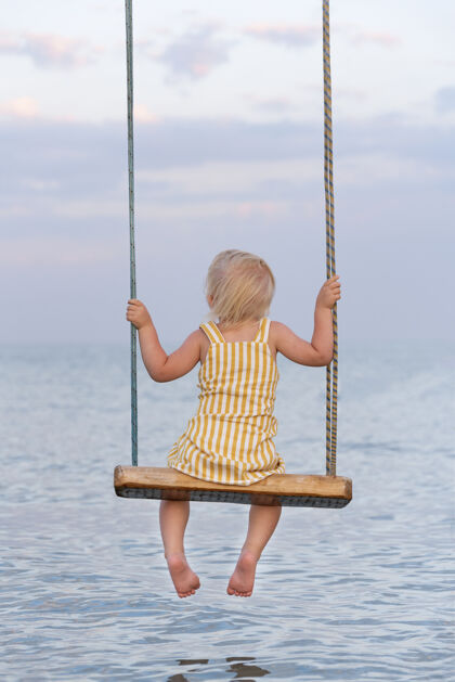 风景蹒跚学步的孩子坐在绳子上荡秋千水背垂直视图框架快乐童年放松幼儿海洋