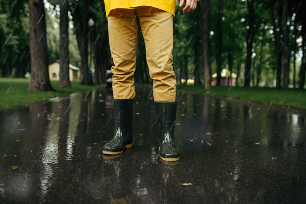 橡胶男子穿着雨衣和胶靴 天气潮湿胡同男人雨中的夏日公园日.水保护 滴滴树枝巷子户外