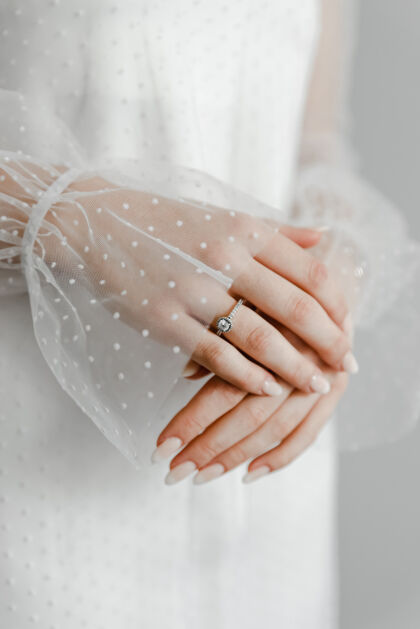 面纱戴灰色围巾的手指上优雅钻戒的特写镜头背景.菱形戒指婚礼戒指手母双手 新娘双手合十新娘女士新娘