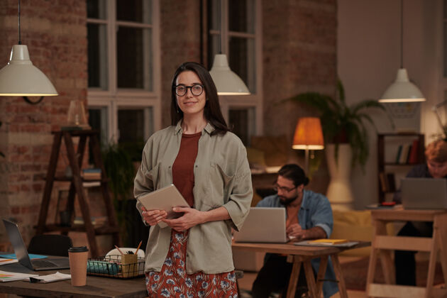 计算机戴眼镜的年轻女设计师的肖像 手持平板电脑 站在办公室前面微笑人员商务人士触摸板