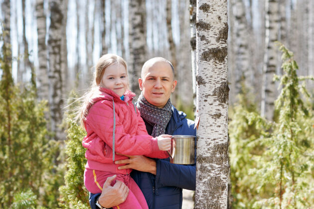 自然一家人在木头里收集一个杯子里的桦树汁肖像树皮女儿