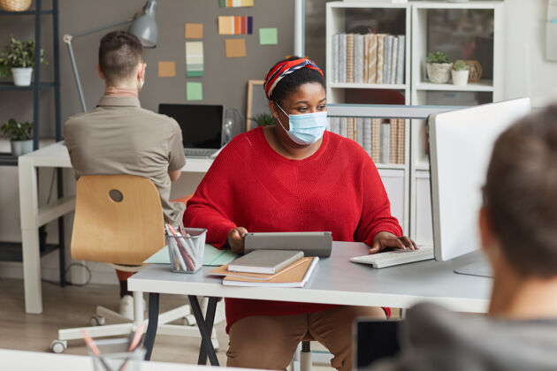 商务女性戴着防护面具的年轻女商人坐在工作场所 和坐在办公室的同事们一起操作电脑办公室人员坐姿