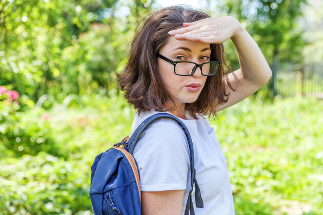 欢呼戴着眼镜 背着背包 在绿色公园背景上微笑的快乐美丽的积极的女学生公园回来秋天