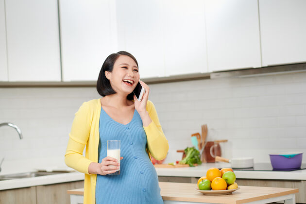 亚洲快乐的孕妇拿着美味的橘子和智能手机交谈女人韩国厨房