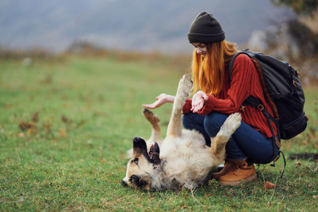 年轻一个背着背包的女远足者在野外和一条狗玩耍山微笑成人