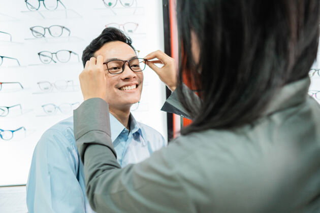 帮助一个女店员在眼镜店给一个男顾客戴眼镜提供眼科医生微笑