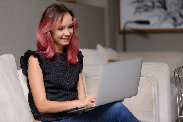 快乐美丽的商人肖像与粉红色的头发使用笔记本电脑在客厅从家办公的概念肖像室内染色