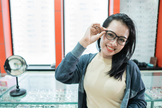 近一个美丽的女人戴着她选择的眼镜 在一家眼科诊所的眼镜橱窗前摆姿势选择亚洲女性