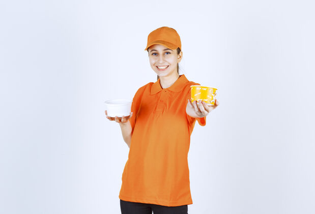 年轻人身着橙色制服的女快递员双手捧着塑料杯和黄色面杯服装休闲食品