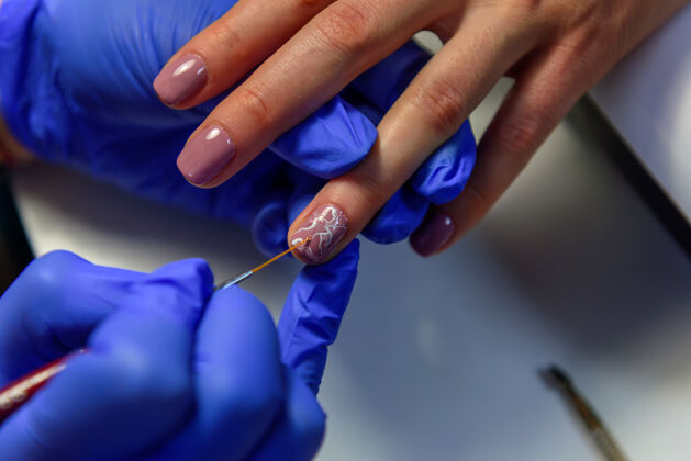 手套在指甲上涂上凝胶油 在指甲上画画美甲师在蓝色手套上涂一层薄薄的清漆刷指甲用柔和的颜色刷子工艺美容师