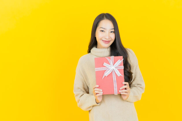 美丽肖像美丽的亚洲年轻女子微笑着黄色墙上的红色礼盒购物节日亚洲