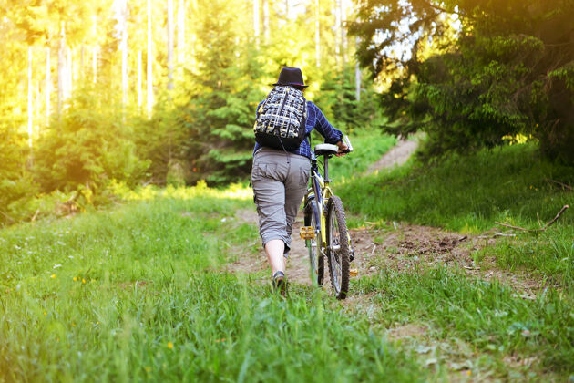 帽子这个女孩夏天在山里的树林里骑自行车自行车背包骑