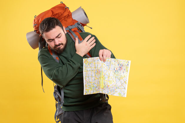 专业顶视图的年轻旅行的家伙背着背包拿着地图和痛苦的肩膀疼痛的黄色微笑地图人