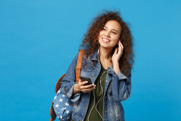 设备年轻的非洲裔美国少女 穿着牛仔服 背着耳机 隔离在蓝色的墙上女性举行T恤