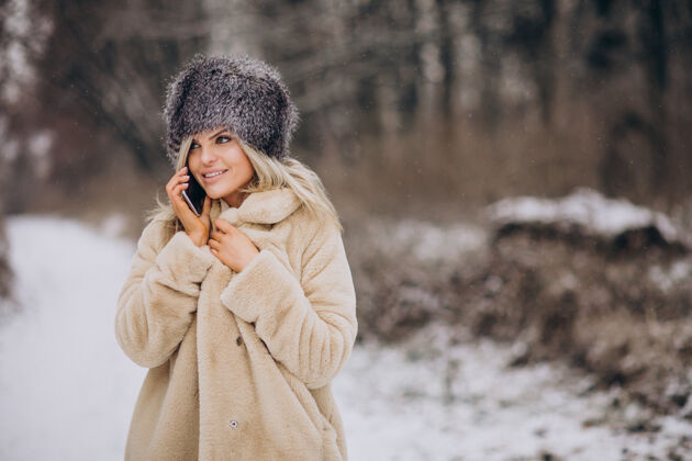 降雪穿着冬衣的女人走在满是雪的公园里打电话树移动探索