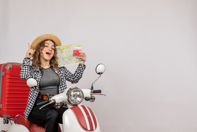 灰色骑着轻便摩托车的年轻女子拿着灰色的卡片和地图 高兴极了人模型摩托车