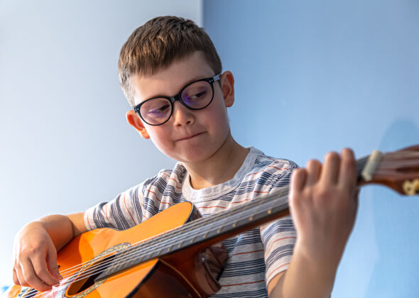 播放器戴眼镜的可爱男孩在家学弹古典吉他吉他学习演奏