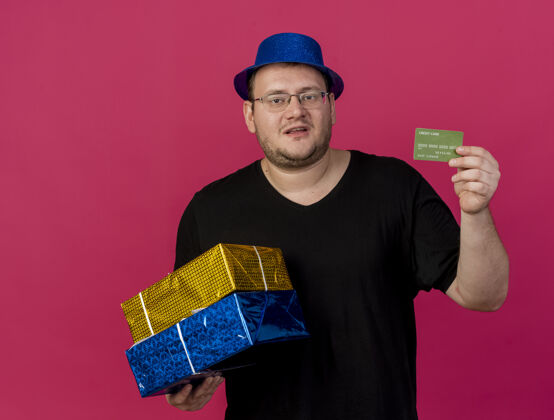 粉色未出租的成年斯拉夫男子戴着眼镜 戴着蓝色派对帽 手里拿着礼品盒和信用卡信用卡空格成人