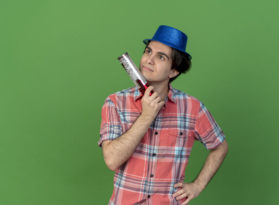 空间体贴英俊的白人男子戴着蓝色的派对帽手持五彩纸屑大炮望着身边思想绿色帽子
