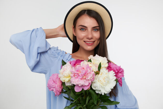 肖像一个快乐的女人 深色的长发 戴着帽子 穿着蓝色的裙子 手里拿着一束花 抚摸着她的头年轻女性女士