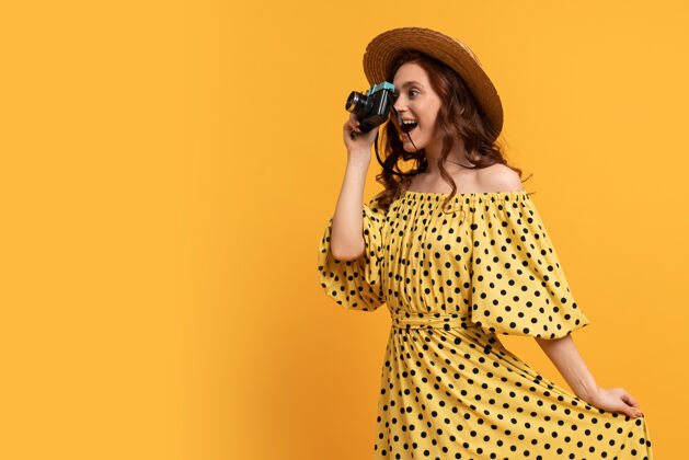 相机戴草帽 穿夏装的旅行妇女在黄色的背景下与复古相机合影衣服潮流女性