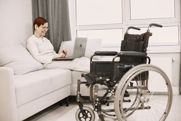 自由职业者残疾人的生活熟女躺在沙发上拿着笔记本电脑退休肖像电话
