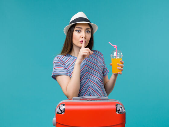 女性前视图：度假中的女人拿着她的红色袋子 蓝色书桌上放着她的果汁旅行旅行度假女人美丽航行举行