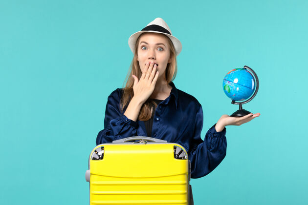 成人前视图年轻女子手持地球仪 在淡蓝色背景上准备度假女性度假旅行海上飞机女性人地球仪
