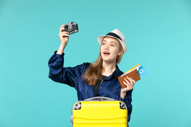欢呼前视图年轻女子手持相机和机票在淡蓝色背景的海上旅行 飞机航行航行成人相机