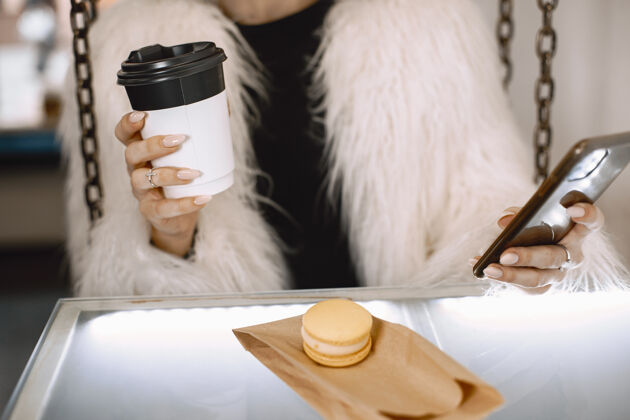 写作黑发女孩穿着白色皮衣的女人拿着电话和咖啡的女人成人肖像咖啡