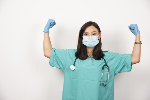 女性戴着面具的女医生在白色背景上展示她的肌肉高质量的照片听诊器医生面罩