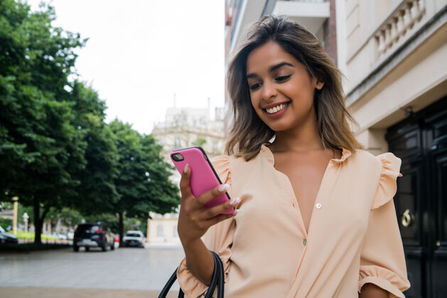 年轻年轻女子在街上户外散步时使用手机的画像人文字乐趣