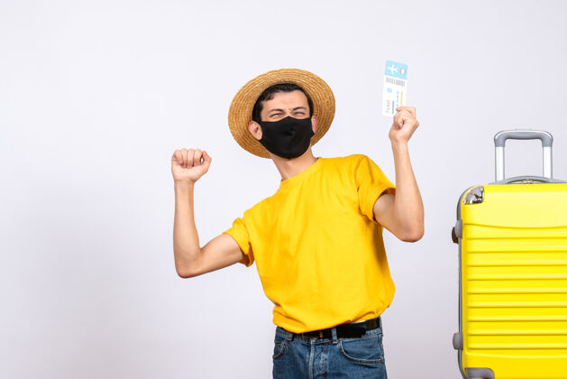 男性正面图身穿黄色t恤的年轻人站在黄色手提箱旁 举着旅行票 表达他的幸福年轻人向上成人