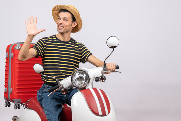 手面带微笑的年轻人 戴着草帽 坐在轻便摩托车上挥舞着手帽子微笑挥手