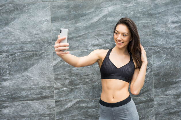 训练健身美女在户外墙前用智能手机在城市里自拍锻炼后分享社交网络年轻手机运动