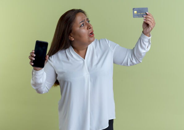 白种人一个心不在焉的白人中年妇女手里拿着电话 看着信用卡电话关心信用
